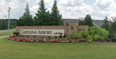 Entrance sign of Carolina Arbors by Del Webb, a 55+ active adult community in Durham, North Carolina, surrounded by landscaped flowers and greenery.