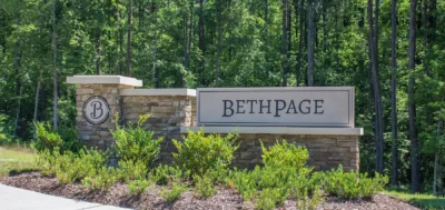 Entrance monument sign for Creekside at Bethpage in Durham, NC, featuring stone pillars, landscaped greenery, and the community name "Bethpage" against a wooded backdrop