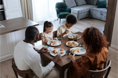 A photograph of a brown-skinned family of four enjoying breakfast together in a bright, modern kitchen in a new construction homes in Triangle NC